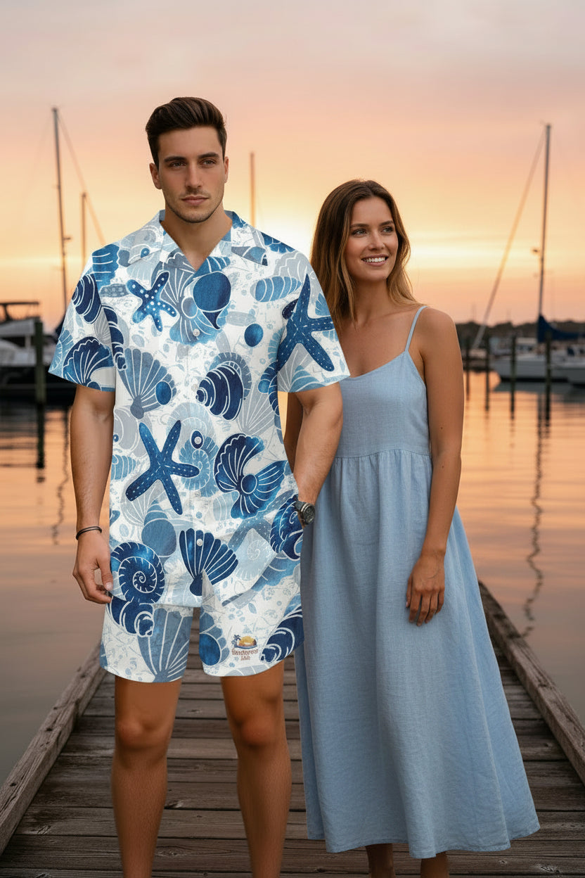 A man wearing a white short-sleeve camp collar shirt and matching shorts set, both featuring a blue ocean-themed print with seashells, starfish, and waves, shown against a plain white background.